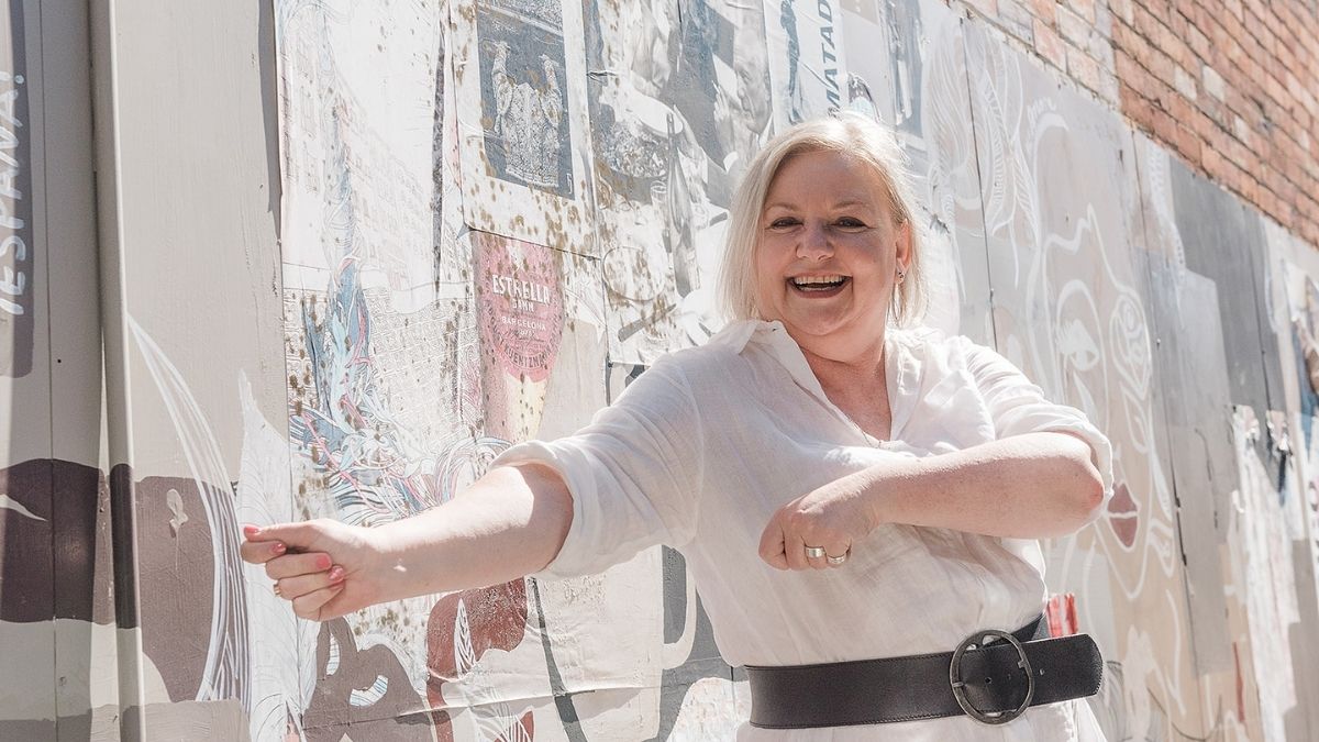 Mell Millgate, founder of Starfish Marketing in Albury Wodonga, smiling in a laneway while gesturing playfully in front of a mural wall.