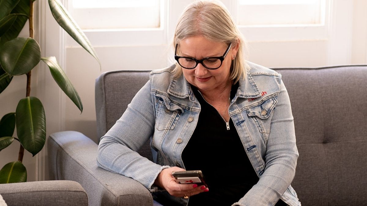 Mell Millgate from Starfish Marketing sitting on a grey couch, wearing glasses and a denim jacket, smiling while looking at her phone.
