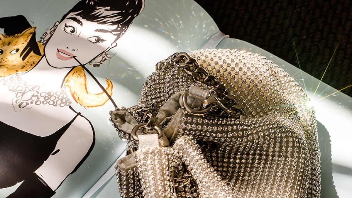 Close-up of a sparkling rhinestone handbag on a magazine illustration of Audrey Hepburn with a cat, representing creativity and visual storytelling in marketing.