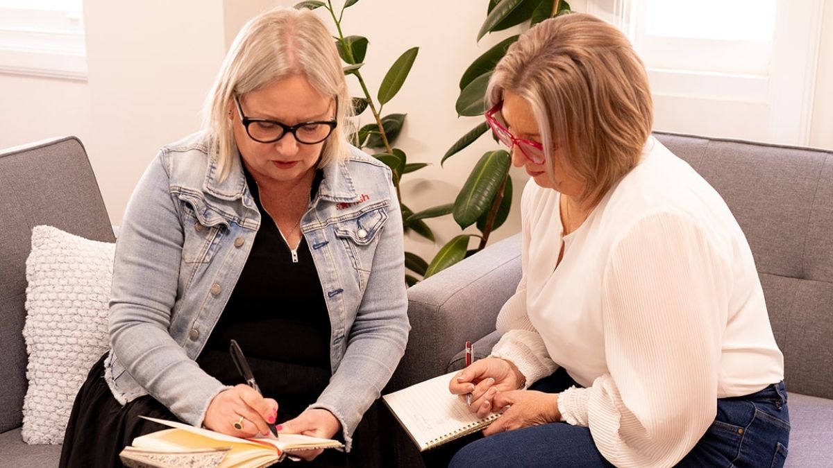 Mell Millgate from Starfish Marketing working with a client, sitting together on a couch reviewing notes and planning marketing strategy.
