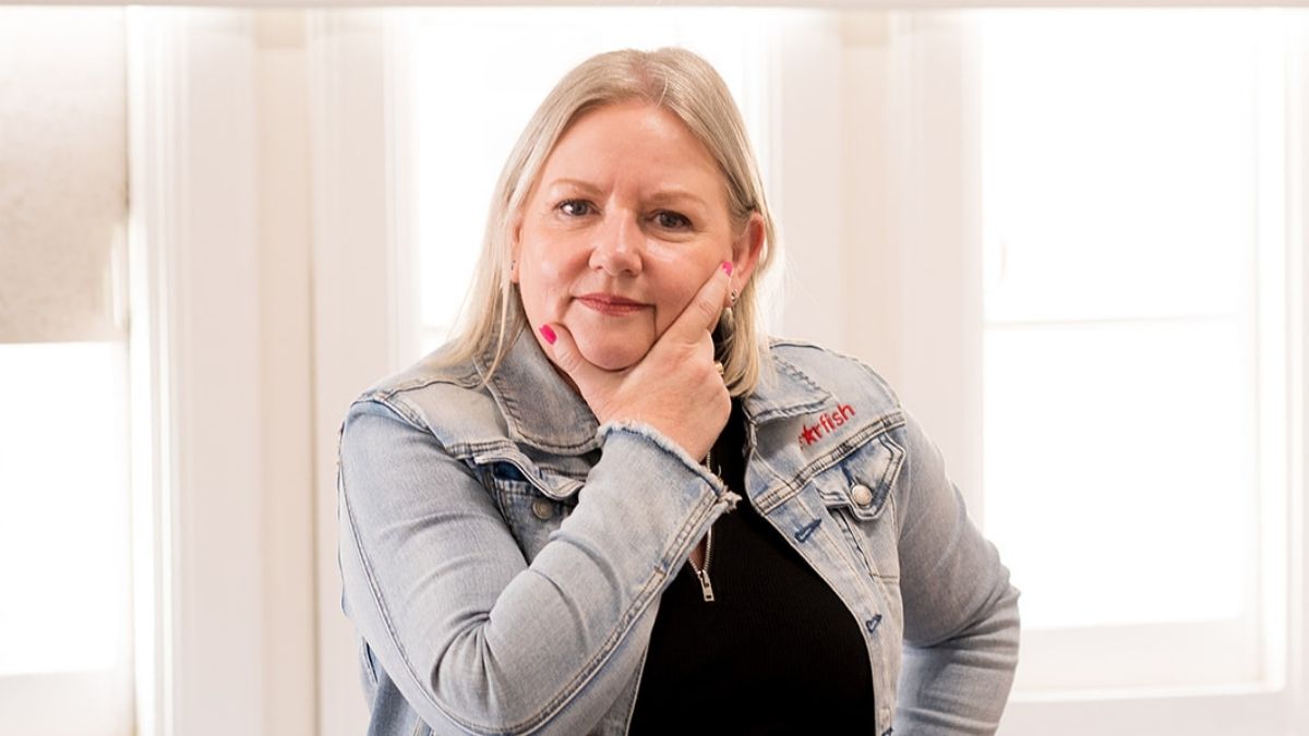 Mell Millgate, founder of Starfish Marketing, standing indoors with hand on chin, wearing a denim jacket and looking thoughtfully at the camera.