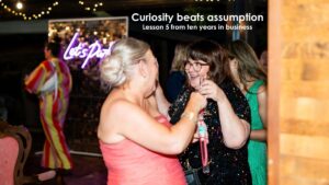 Two women laughing and talking at a business event, representing curiosity, conversation and connection in business relationships.