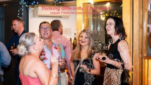 Business people chatting and laughing at a celebration event while one person blows bubbles, representing different perspectives, connection and business positioning.