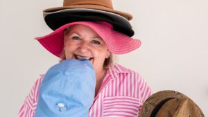 Mell from Starfish Marketing smiling while wearing several stacked hats and holding another, representing different marketing roles a business can choose from.