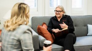 Mell Millgate from Starfish Marketing sitting on a grey sofa, smiling and talking with another woman during a one on one business conversation.